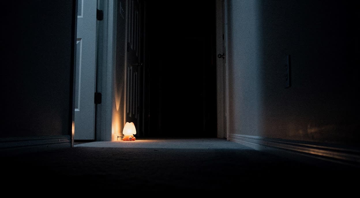 A child’s nightlight glowing at the far end of a long dark hallway